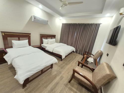 a hotel room with two beds and a chair at Regency Guest House Peshawar in Peshawar