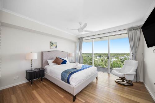 a bedroom with a bed and a chair and a window at Pelican Waters Golf Resort Sunshine Coast in Caloundra