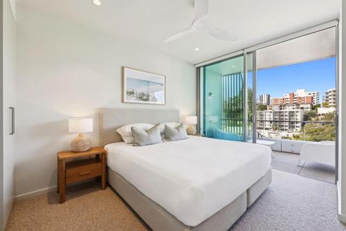 a white bedroom with a bed and a large window at Miles at Kirra Point 604 in Gold Coast