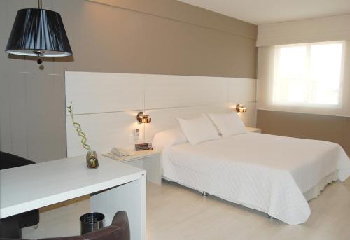 Schlafzimmer mit einem weißen Bett, einem Schreibtisch und einem Bett in der Unterkunft Hotel Manta in Pelotas