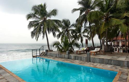 a swimming pool next to the ocean with palm trees at 36 Palms Boutique Retreat in Cherai Beach
