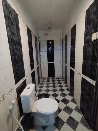 a bathroom with a toilet and a black and white checkered floor at NS Apartments in Dalugama