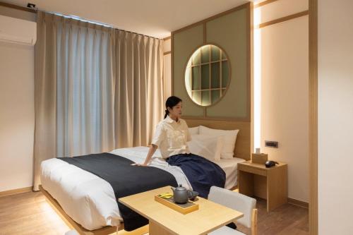 a woman sitting on a bed in a hotel room at Anook Ryokan Hotel Daejeon Daeheung in Daejeon