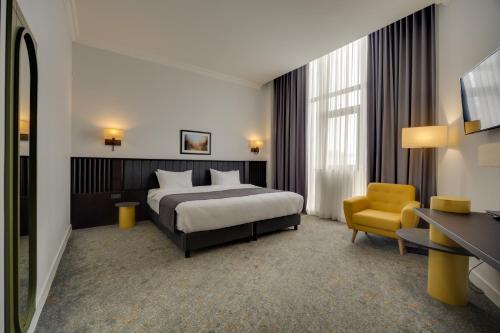 a hotel room with a bed and a yellow chair at Pine Astoria Hotel in Tbilisi City