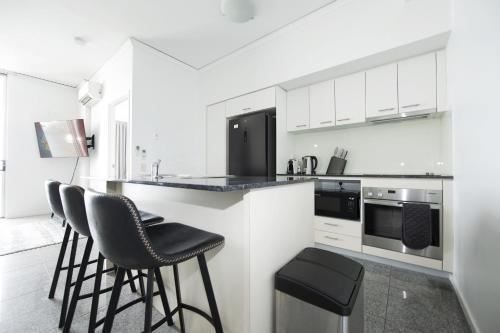 a kitchen with white cabinets and black appliances at Rooftop Apartment - Heated Pool & Beach access in Marcoola