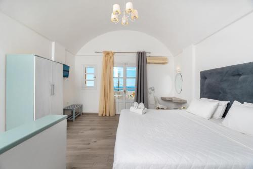 a white bedroom with a large bed and a bathroom at Maistros Village Santorini - Anamar Collection in Karterados