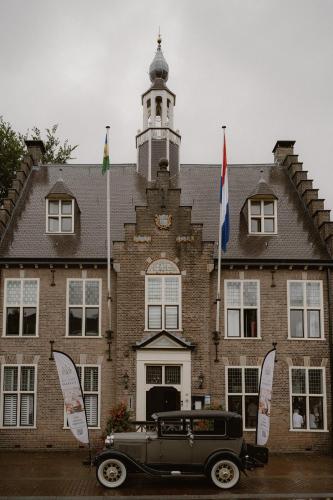 an old car parked in front of a building with flags at Luxe appartement in het hart van Castricum in Castricum