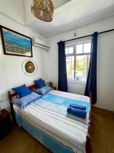 a bedroom with a bed with blue pillows and a window at La Villa Allamanda in Rodrigues Island