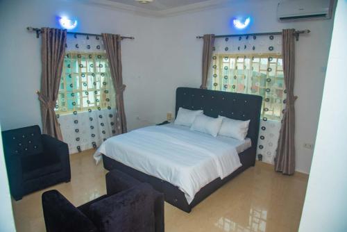 a bedroom with a bed and a chair and two windows at Classic Hills Hotel & Resort in Uyo