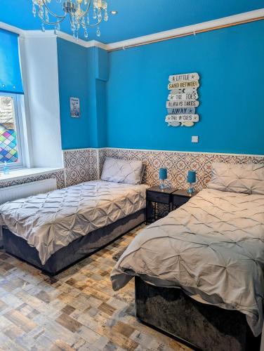 two beds in a room with blue walls at Commodore Guesthouse, Seaside Holiday Suites in Rothesay