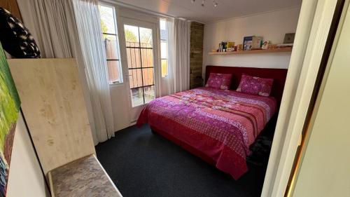 a bedroom with a bed with a red comforter and two windows at Janka B&B in Elim