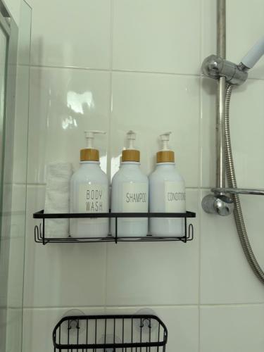 four bottles of soap and towels on a shelf in a bathroom at Roseus and Mimosa Cottages in Combe Martin