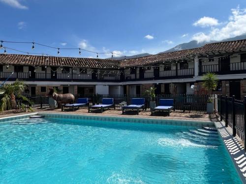 a swimming pool in front of a hotel with chairs and a horse at Hotel Aceitunos in Villa de Leyva