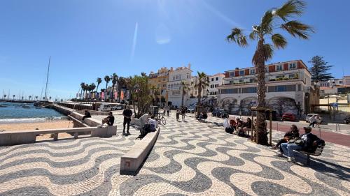 people sitting on benches on a sidewalk next to the beach at Cozy one bedroom apartment in the heart of Cascais historic center in Cascais