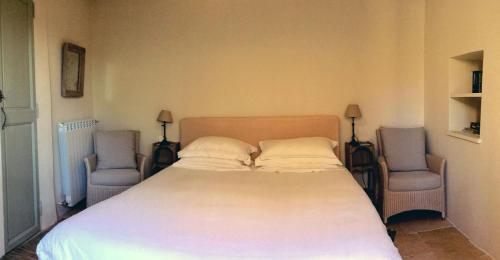 a bedroom with a large bed with two chairs at Ancienne Maison des Gardes in Lourmarin