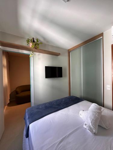 a bedroom with a white bed and a flat screen tv at Flat em Brasilia - Parque do Sudoeste in Brasília