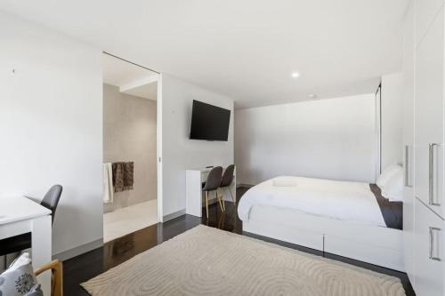 a white bedroom with a bed and a tv at Modern Beachside Studio in Kingston Beach