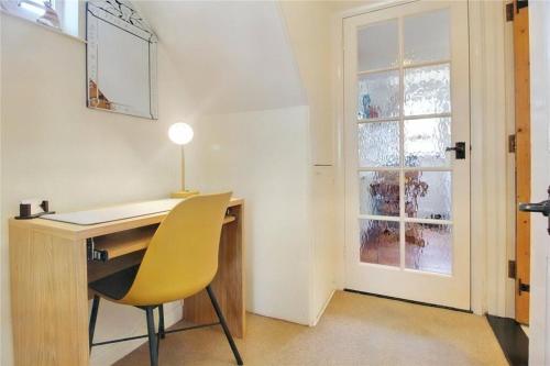 a desk with a yellow chair next to a window at Loom Cottage in Southwold