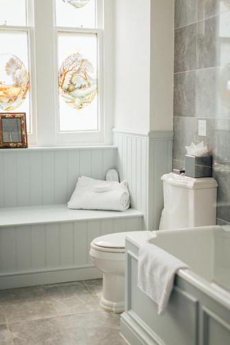 a white bathroom with a toilet and two windows at Beechfield House in Beanacre