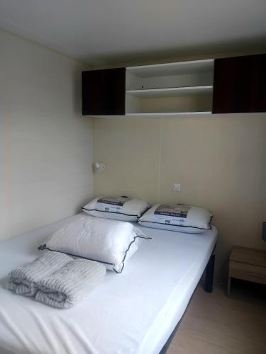 a white bed with two pillows on top of it at Le mobil home bleu ! Camping Naturiste in Montalivet-les-Bains
