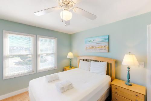 a bedroom with a bed with a ceiling fan and two windows at Sandcastle in Corolla