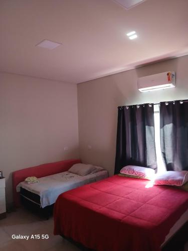 a bedroom with two beds and a window with a red blanket at Casa PA parque das aguas in Bonito