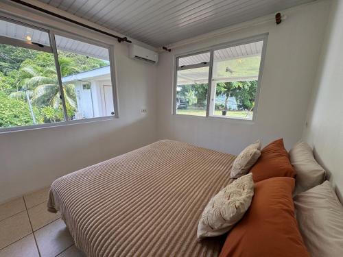 a bedroom with a bed with pillows and two windows at Grand Panorama Villa in Tahaa