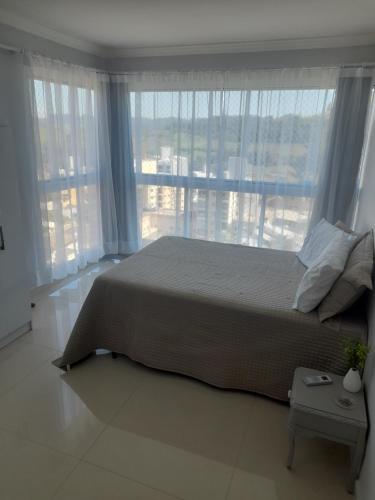 a bedroom with a large bed and large windows at Ap 503 Ed Brisa do sol em Piratuba in Piratuba