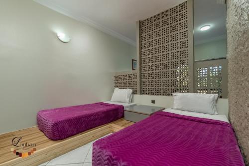 two beds in a room with purple sheets at Hôtel Résidence Louban in Agadir