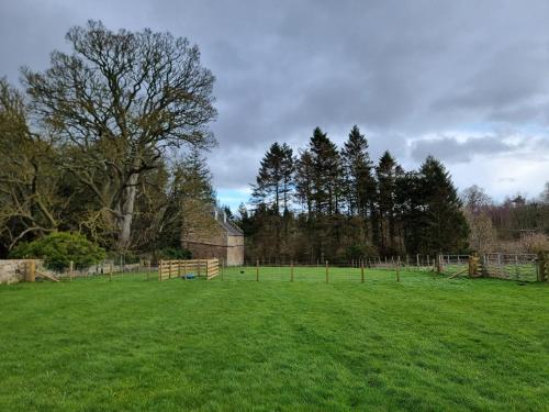 a large green field with a fence and trees at Midhope Castle Cottages in Queensferry