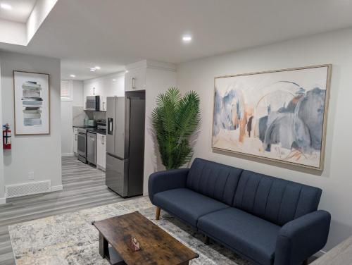 a living room with a blue couch and a kitchen at Calgary Serene Suite - 19mins from airport, 1hr to Banff, 85" Cinema, Fibre WiFi, Full Kitchen in Calgary