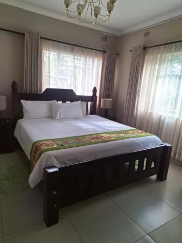 a bedroom with a large bed with white sheets and windows at Eastview Guest House in Harare