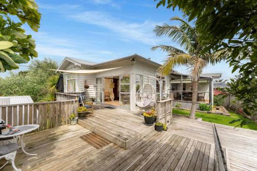 a house with a wooden deck with a patio at Cabbage Tree Cottage in Papamoa