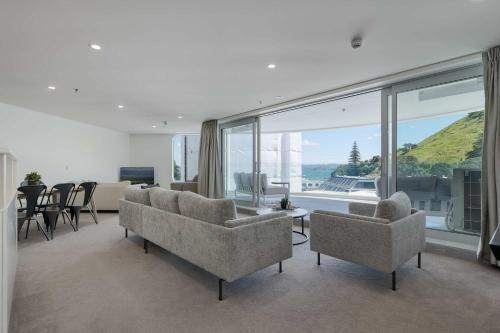 a living room with couches and chairs and a large window at Oceanside Belle in Mount Maunganui