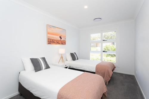 two beds in a white room with a window at Casa Azul in Burrill Lake