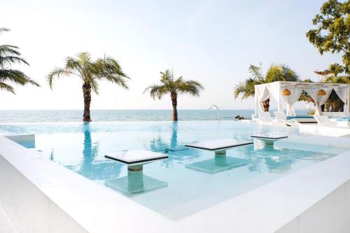 a pool with tables and the ocean in the background at Pure Sunset Beach - By Mikihollick in Na Jomtien