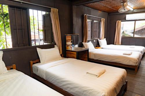 a room with three beds and a tv and windows at Vang Vieng Ban Lao Guesthouse in Vang Vieng