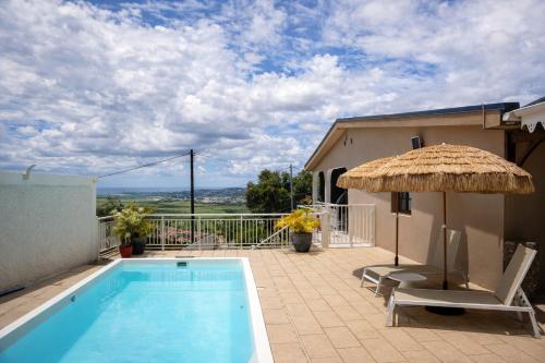 a swimming pool with a straw umbrella and a chair and an umbrella at Le cocon de Josie avec Jacuzzi & Piscine Privée, Le Lamentin, Martinique in Le Lamentin