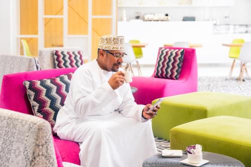 a man sitting on a couch looking at his cell phone at Mercure Sohar in Sohar