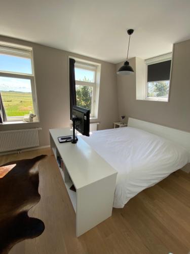 a bedroom with a white bed and a desk with a computer on it at Oomes Huus - Sleep by Hästens, Wake with Coffee in Den Hoorn
