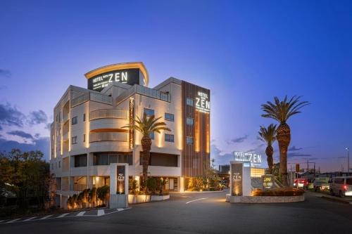 a hotel with palm trees in front of a building at HOTEL ZEN RIKYU Chiba Shiroi in Shiroi