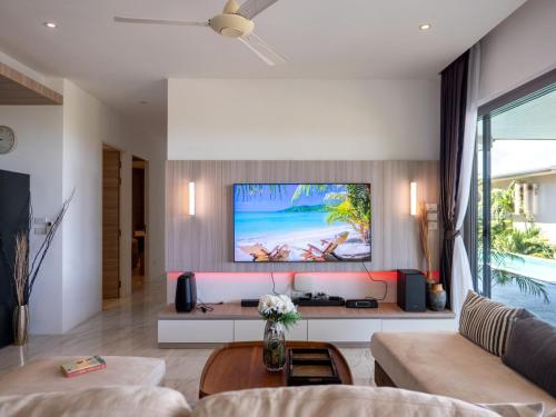 a living room with a couch and a tv on a wall at Luxe 4BR Sunset Seaview Villa Private Infinity in Plai Laem