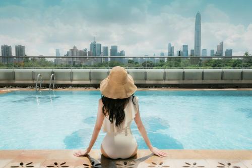 a woman in a hat sitting next to a swimming pool at JW Marriott Hotel Shenzhen in Shenzhen