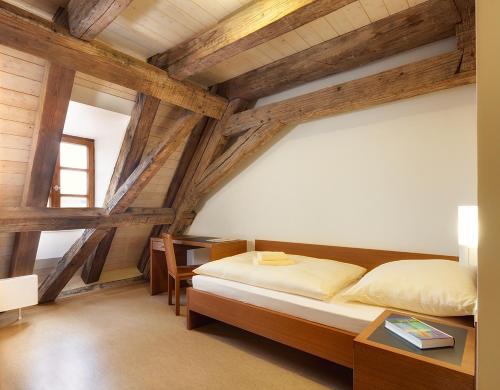 a bedroom with a bed and a desk and wooden ceilings at Gäste- und Tagungshaus Benediktinerabtei Plankstetten in Berching