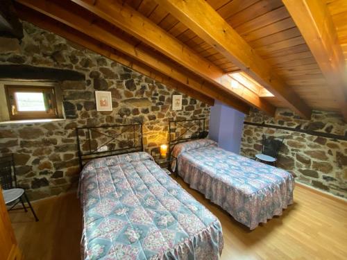 two beds in a room with a stone wall at Apartamentos La Barcenilla in Herada