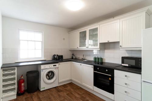 a kitchen with white cabinets and a washer and dryer at Bright 1 Bed Harbour-side Apartment with Balcony in Whitehaven