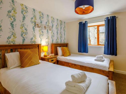 two beds in a bedroom with blue curtains and a window at 2 Bed in Ilfracombe oc-rugga in Berrynarbor