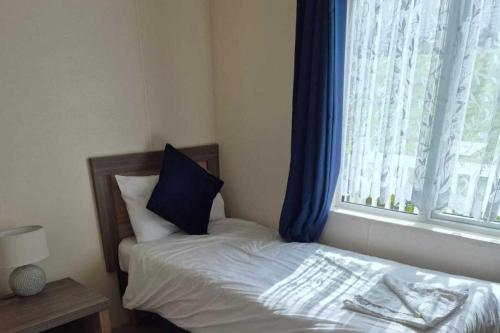 a bed with a blue pillow and a window at 2 Bed Caravan - Sleeps 6 - Pets - Pool - Parking in Newquay