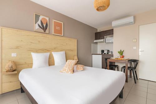 a bedroom with a large white bed and a kitchen at Appart'City Confort Toulouse Aéroport Cornebarrieu in Cornebarrieu
