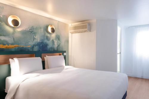 a bedroom with a white bed and a painting on the wall at Kyriad Argenteuil in Argenteuil